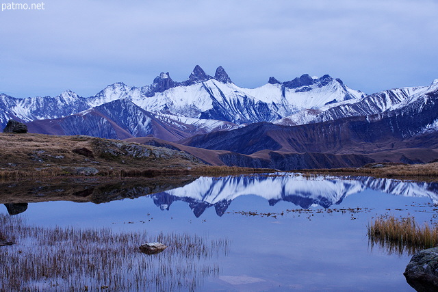 Image of Aiguilles d'Arves mountains partially covered in snow and their reflection on lake Guichard