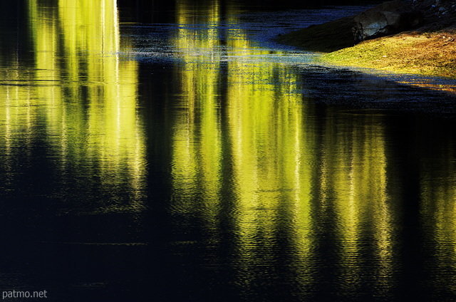 Picture of some yellow reflections on the black water of Montriond lake